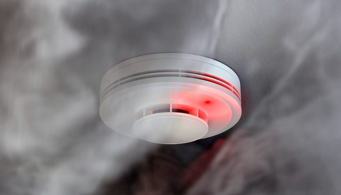 White plastic fire alarm smoke detector with red LED indicator on ceiling. 3D illustration